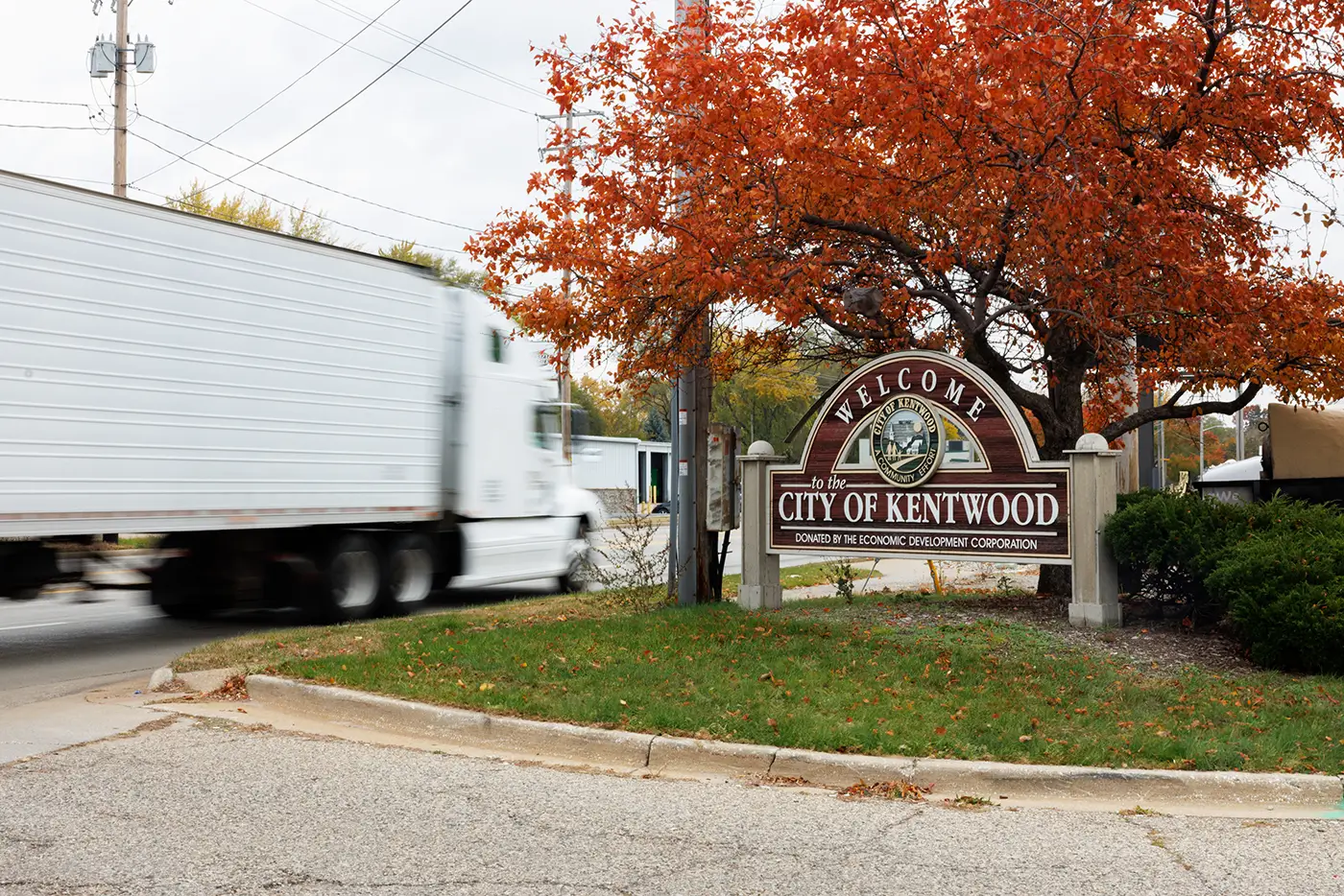 A semi-truck drives along a Kentwood road near the city welcome sign, showing the area served by a truck accident attorney in Kentwood.