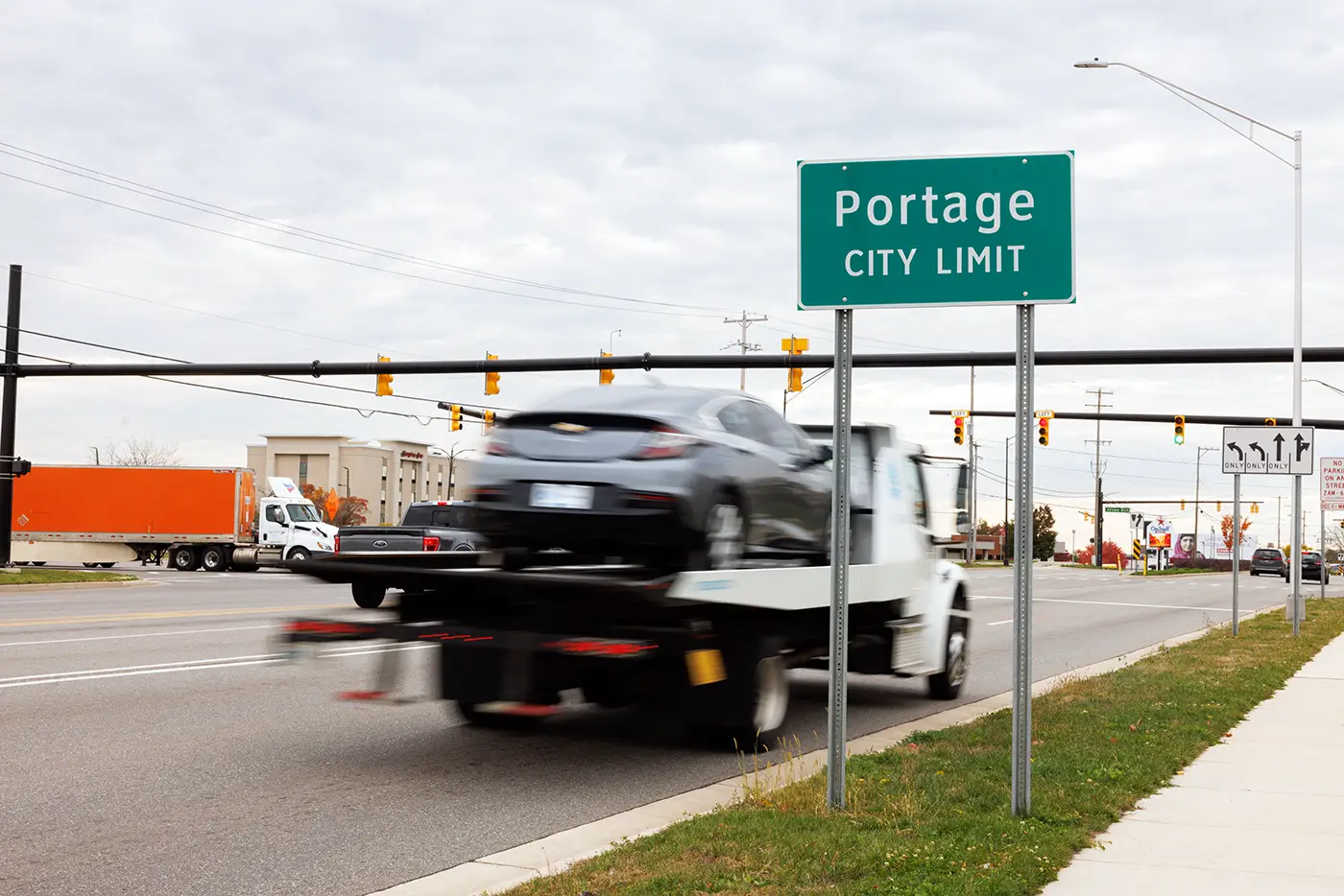 Tow truck driving past the Portage city limit sign, illustrating a busy local road served by a Portage truck accident attorney.