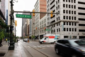 Busy downtown Detroit street with passing cars & city buildings, representing the area served by Michigan Auto Law, a car accident lawyer in Detroit.