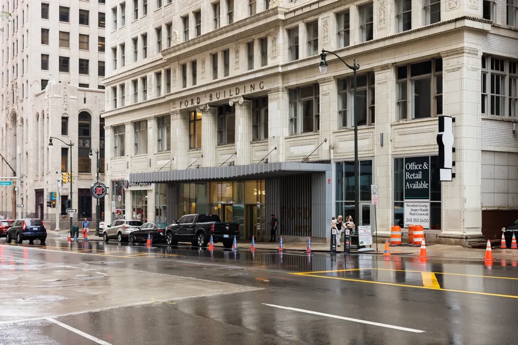 Cars line a wet downtown Detroit street outside the Ford Building, where Michigan Auto Law helps crash victims as a car crash lawyer in Detroit.