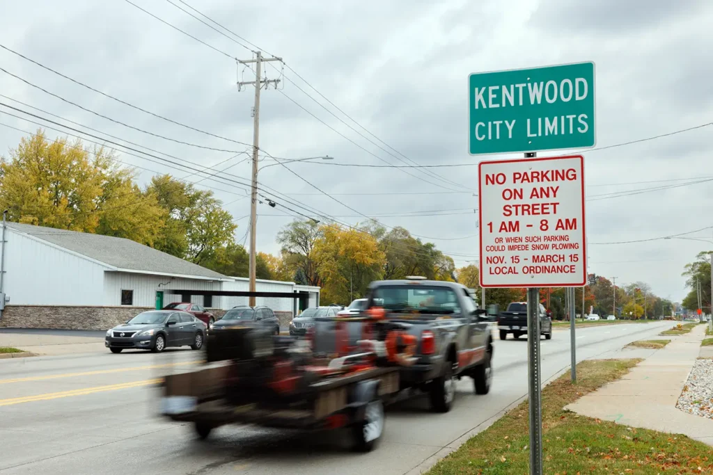 Cars and a pickup pass the Kentwood city limits sign, where Michigan Auto Law serves as a car crash lawyer in Kentwood.