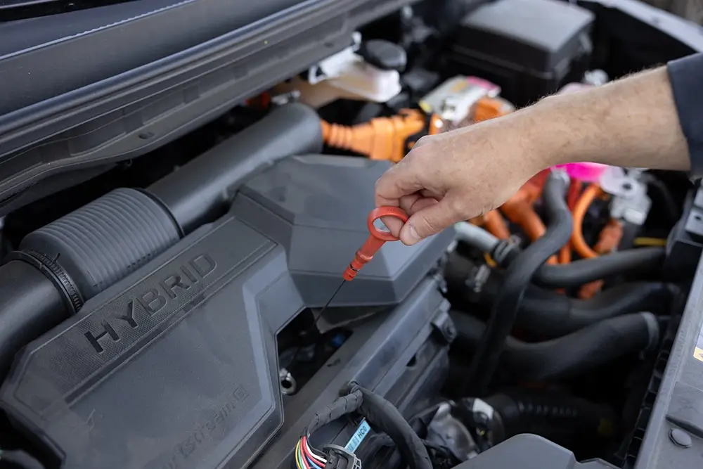 Driver checking engine oil as part of a road trip car checklist.