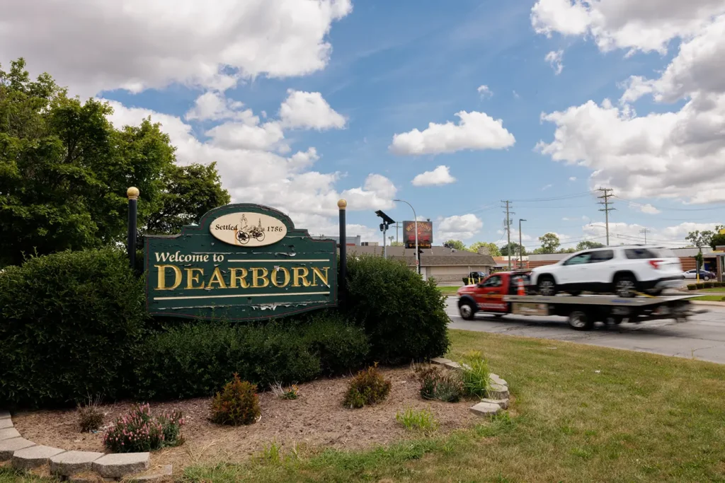 Tow truck drives past the Welcome to Dearborn sign, where Michigan Auto Law handles truck accident lawyer cases.
