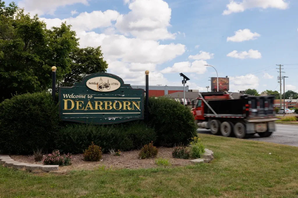 A dump truck drives past the Dearborn welcome sign, where Michigan Auto Law helps crash victims as a truck crash lawyer in Dearborn.