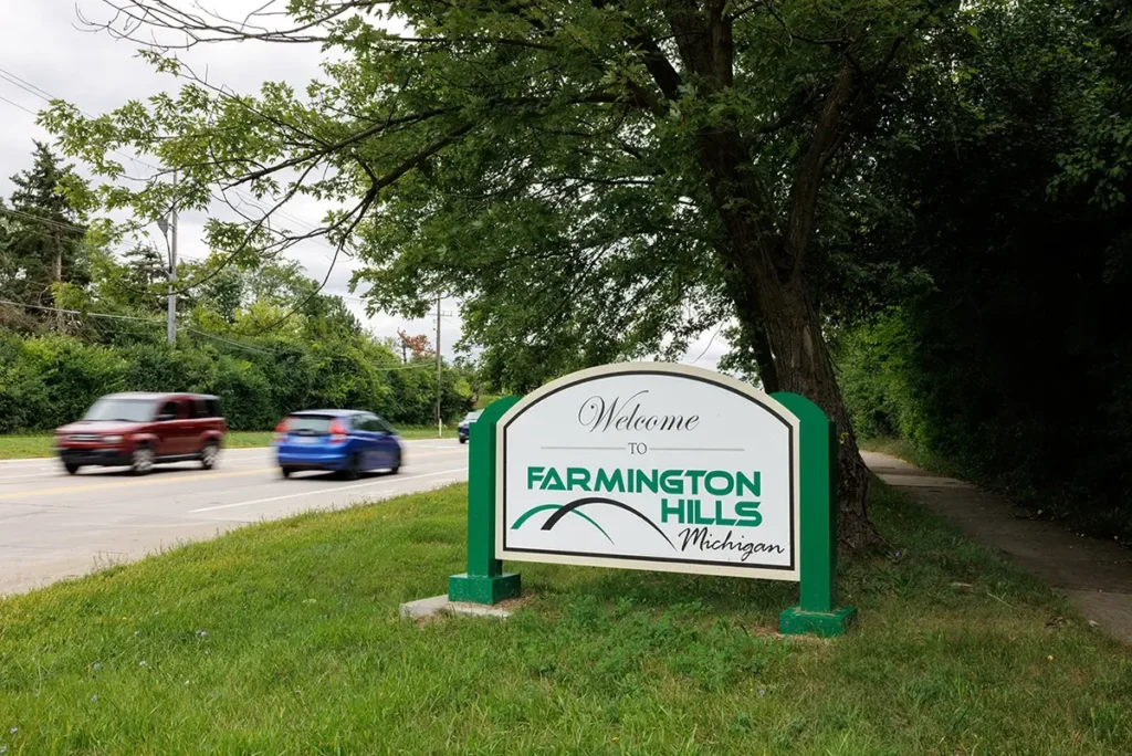 Vehicles pass the Welcome to Farmington Hills sign, representing Uber accident attorney, Michigan Auto Law.
