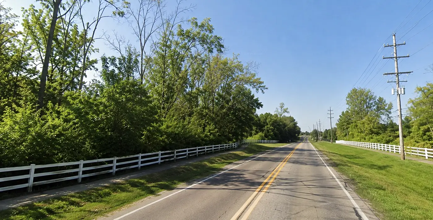 Scenic roadway bordered by trees and white fences, representing Uber accident lawyer Farmington Hills services.