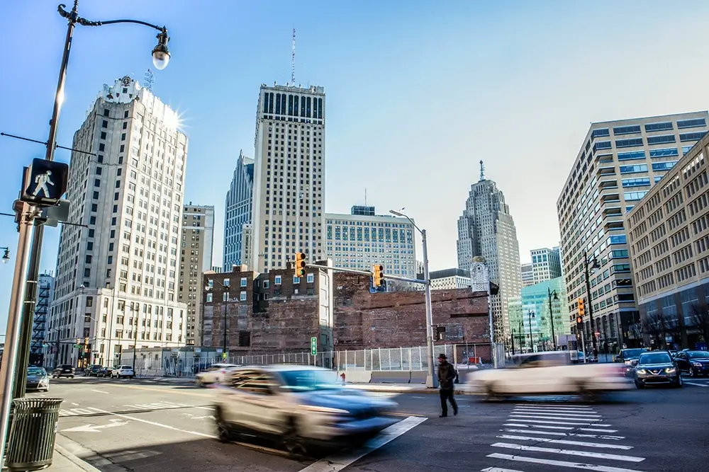 Downtown Detroit intersection with passing traffic and a pedestrian, representing the area served by Michigan Auto Law's pedestrian accident law firm.